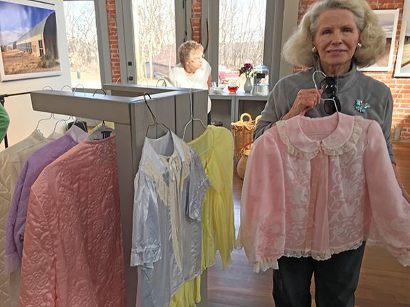 A woman is holding a pink shirt in front of a rack of clothes.