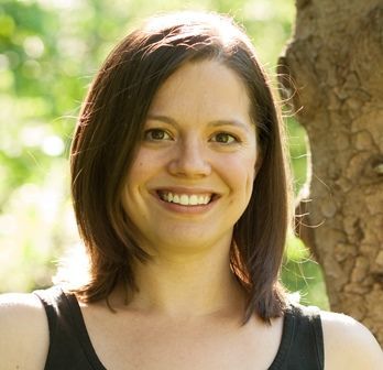 Woman with brown hair smiles outdoors, wearing a black top.