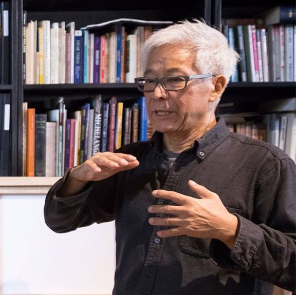A man wearing glasses is standing in front of a bookshelf