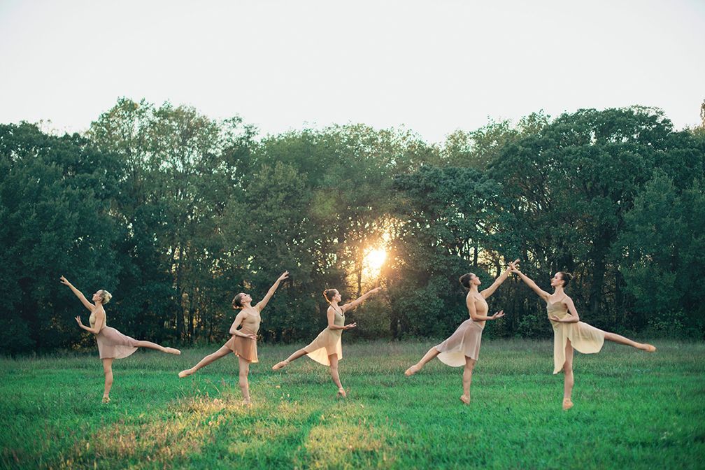 A group of ballerinas are dancing in a field.