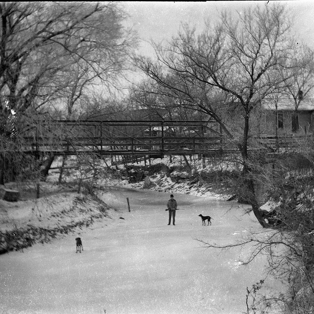 A black and white photo of a man ice skating with two dogs