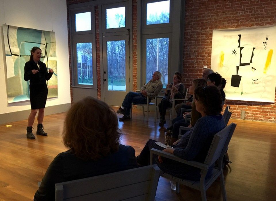 A woman is standing in front of a group of people sitting in chairs in a room.