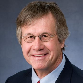 A man wearing glasses and a suit is smiling for the camera.