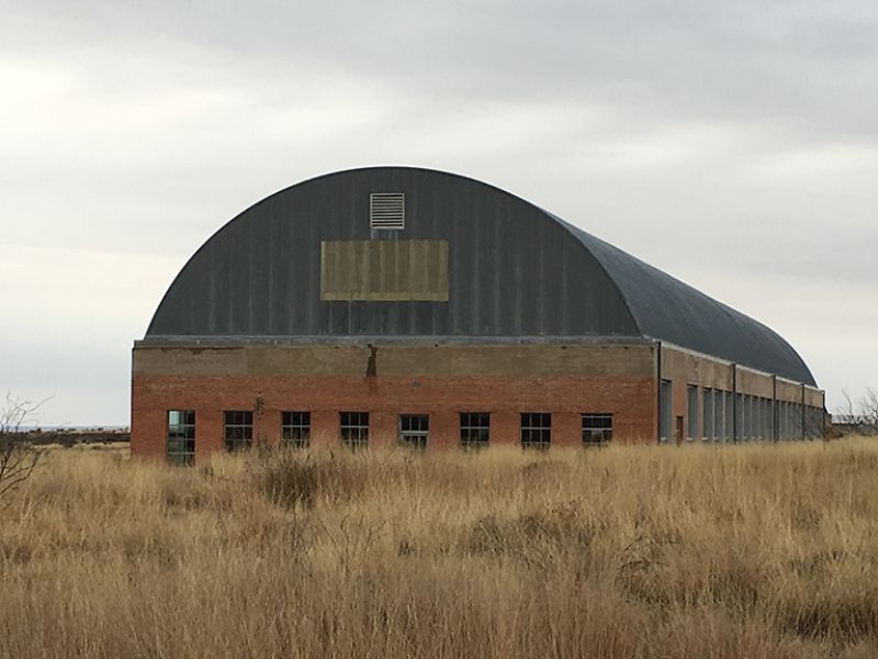 A large building with a curved roof is in the middle of a field
