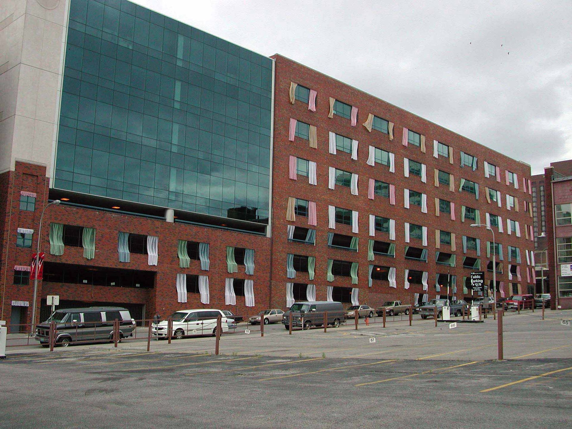 Modern red brick building with glass panel and many open windows; vehicles parked in front.