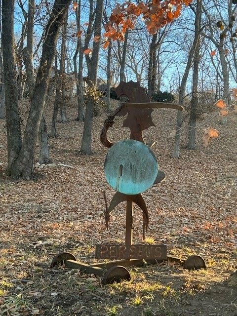 A metal sculpture of a person playing a stringed instrument, in a forest setting.