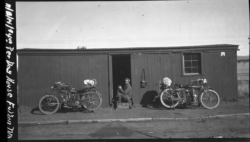 A black and white photo of two motorcycles parked in front of a building