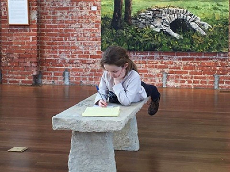 A little girl is laying on a stone bench writing on a piece of paper.