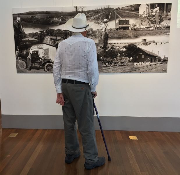 A man with a cane is looking at a picture on a wall