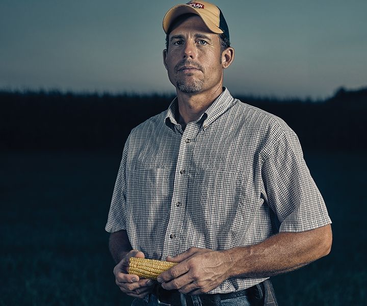 A man in a plaid shirt is holding a corn on the cob