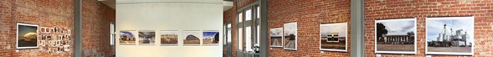 A row of paintings are hanging on a brick wall in a museum.