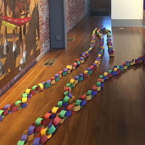 Colorful paper chains on a wooden floor, leading through a room with a painting and exposed brick.