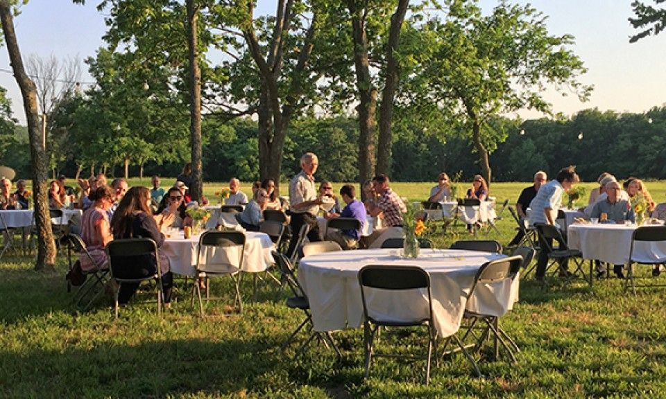 A group of people are sitting at tables in a field.