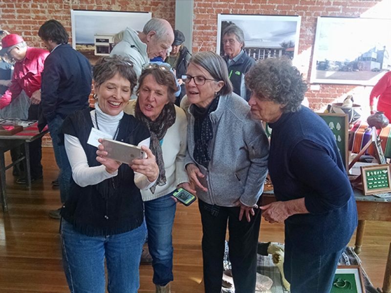 A group of women are standing in a room looking at a tablet.