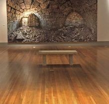 There is a bench in the middle of the room in front of a brick wall.