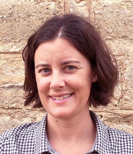 A woman in a plaid shirt is smiling in front of a stone wall.