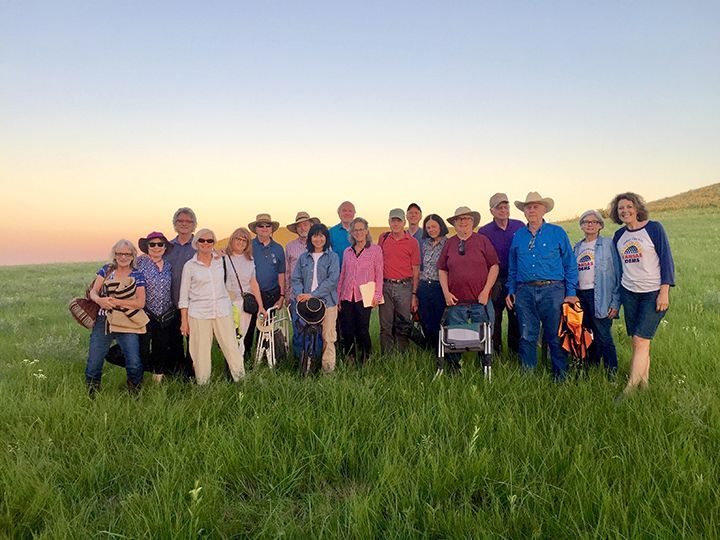 Group of people outdoors in grassy field at dusk. Some wearing hats, smiling.