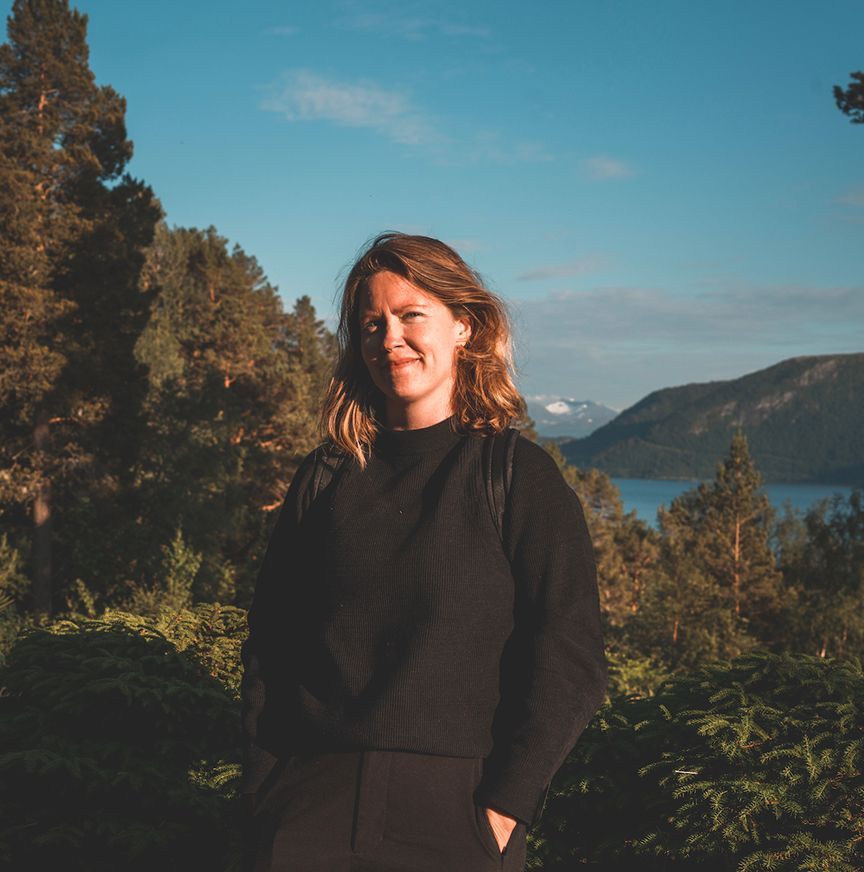 A woman in a black sweater is standing in front of a lake.