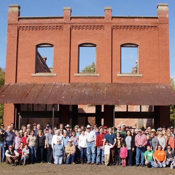 Large group of people in front of a brick building with open window frames and a rusty metal awning.