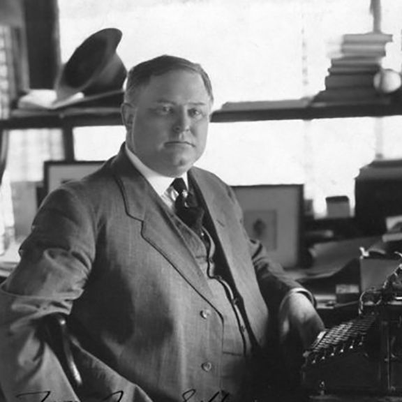 A man in a suit and tie is standing in front of a typewriter