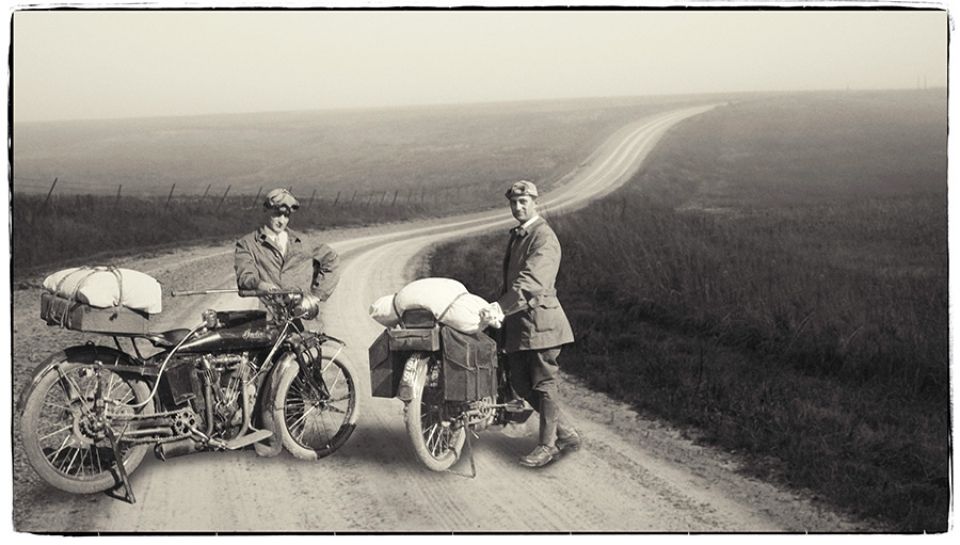Two men standing next to a motorcycle on a dirt road