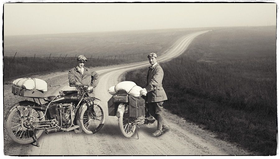 Two men standing next to a motorcycle on a dirt road