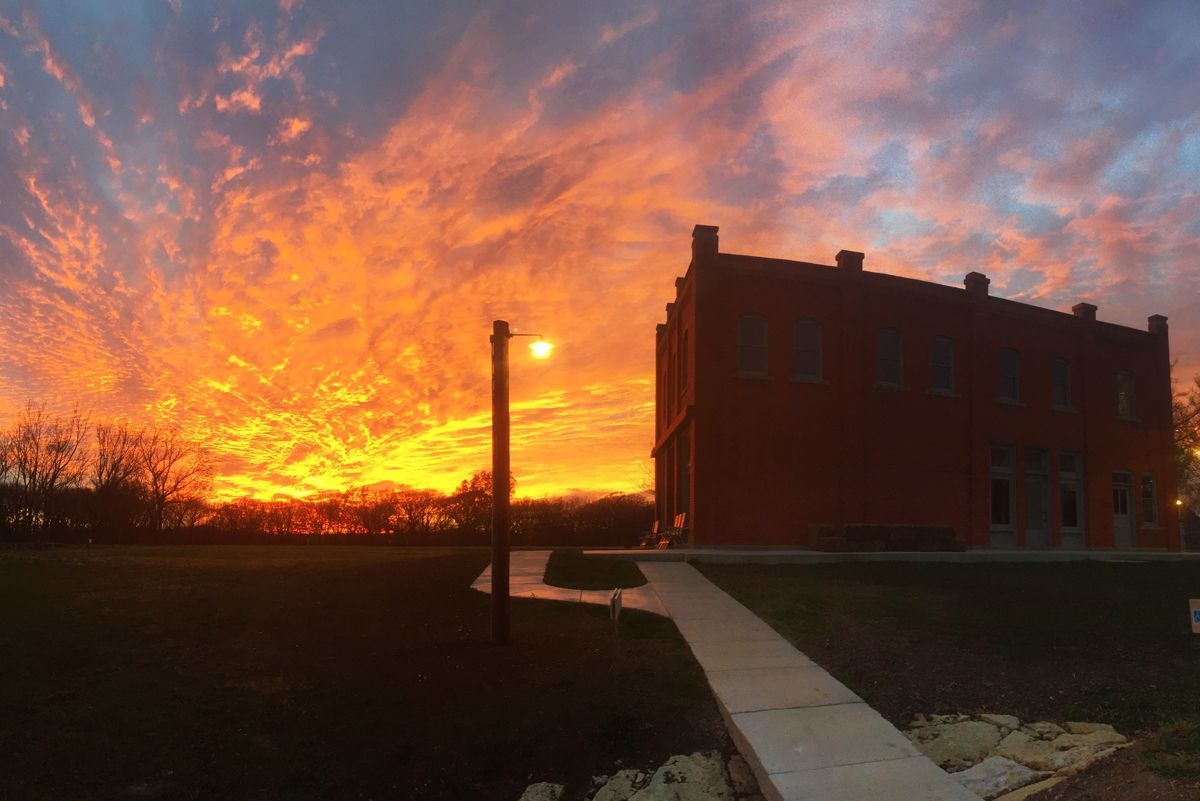 Fiery orange sunset behind a brick building and a lone lamppost.