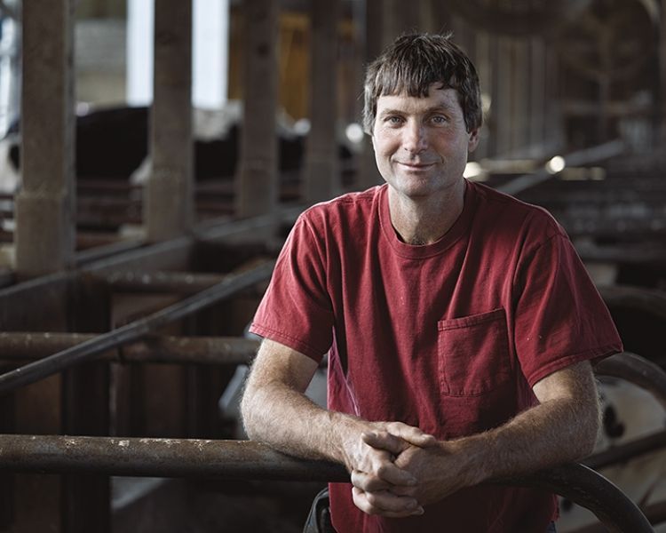 A man in a red shirt is leaning on a railing in a barn.