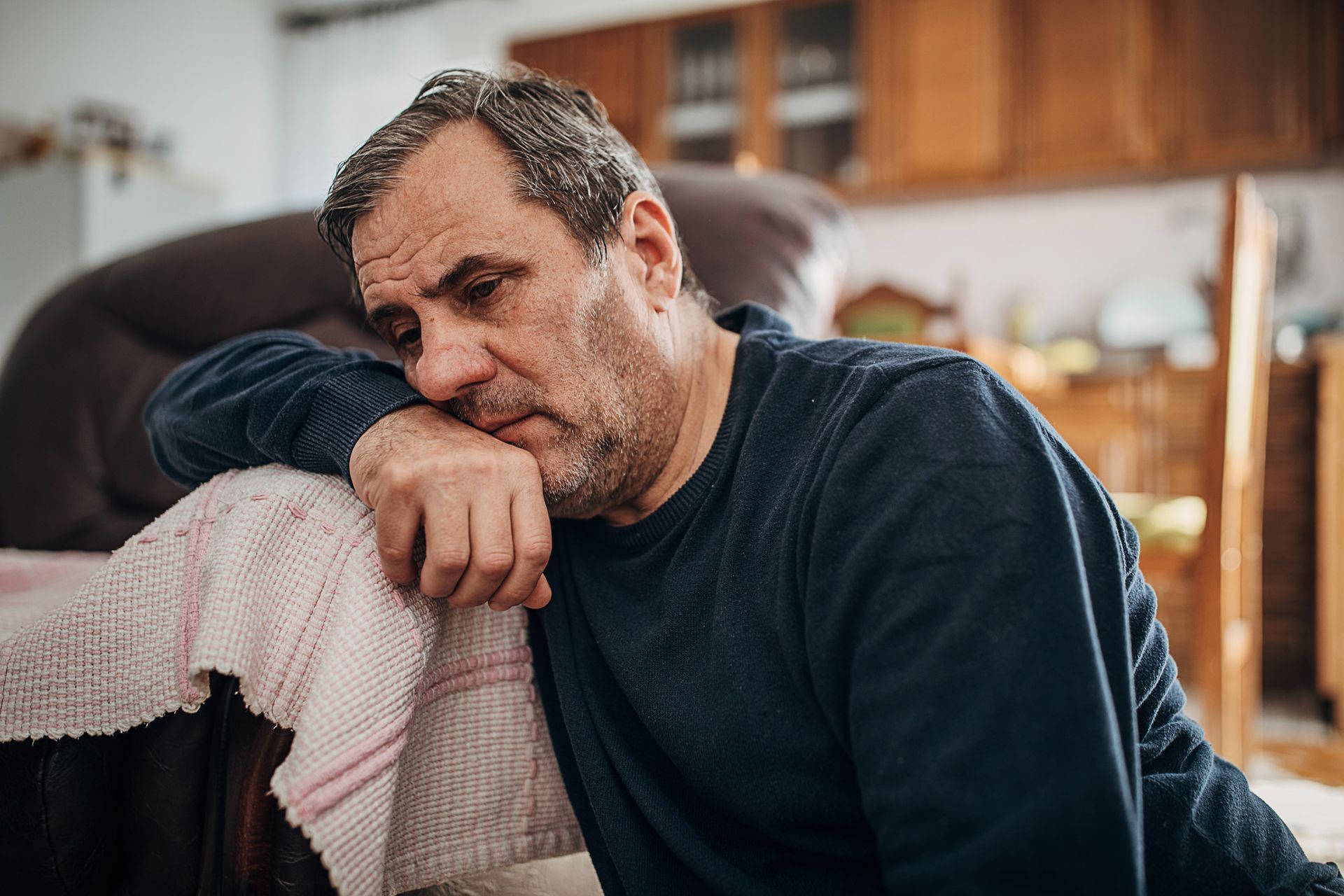 An older man is laying on the floor leaning on a couch.