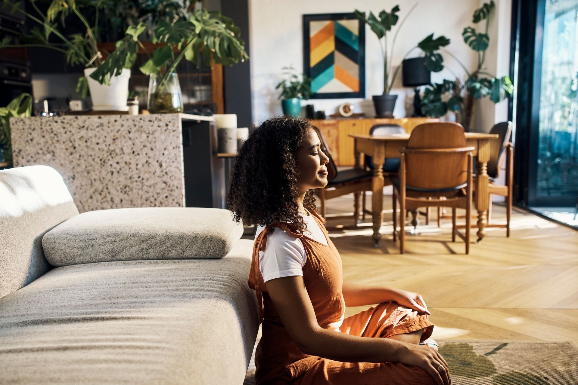 A woman is sitting on the floor in a living room with her eyes closed.