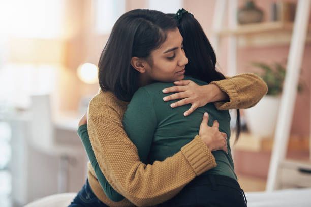 Two women are hugging each other in a living room.