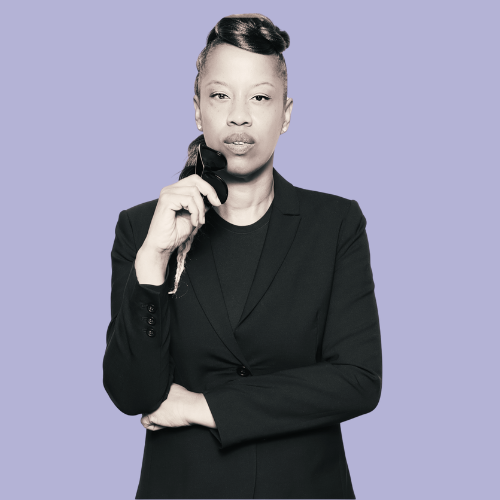 Angela Scarlett in a black suit, holding phone, thoughtful expression, arm crossed.