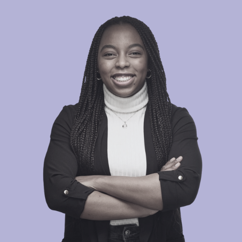 Rey Lambie with arms crossed, wearing a black blazer and white turtleneck, smiling.