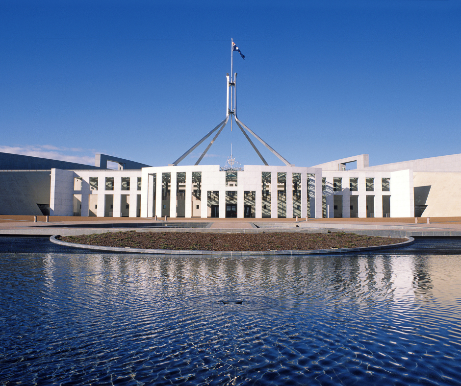 Australian Parliament House with flag on a sunny day reflected in a pool.
