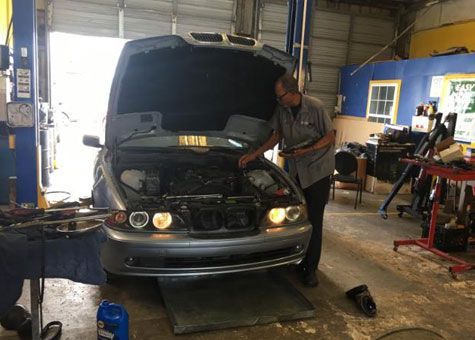 Mechanic inspecting a car engine in a garage. Car is gray, garage has open door.