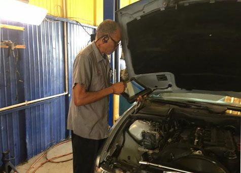 Mechanic in a garage using a tablet to diagnose a car engine.