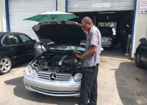 Mechanic inspecting car engine with open hood outside garage.
