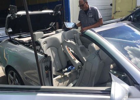 A mechanic works on a silver convertible car with the top down.