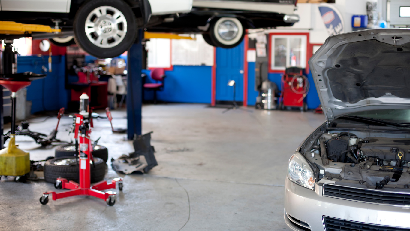 Car repair shop interior with car on lift, another with hood open. Tools and equipment visible.