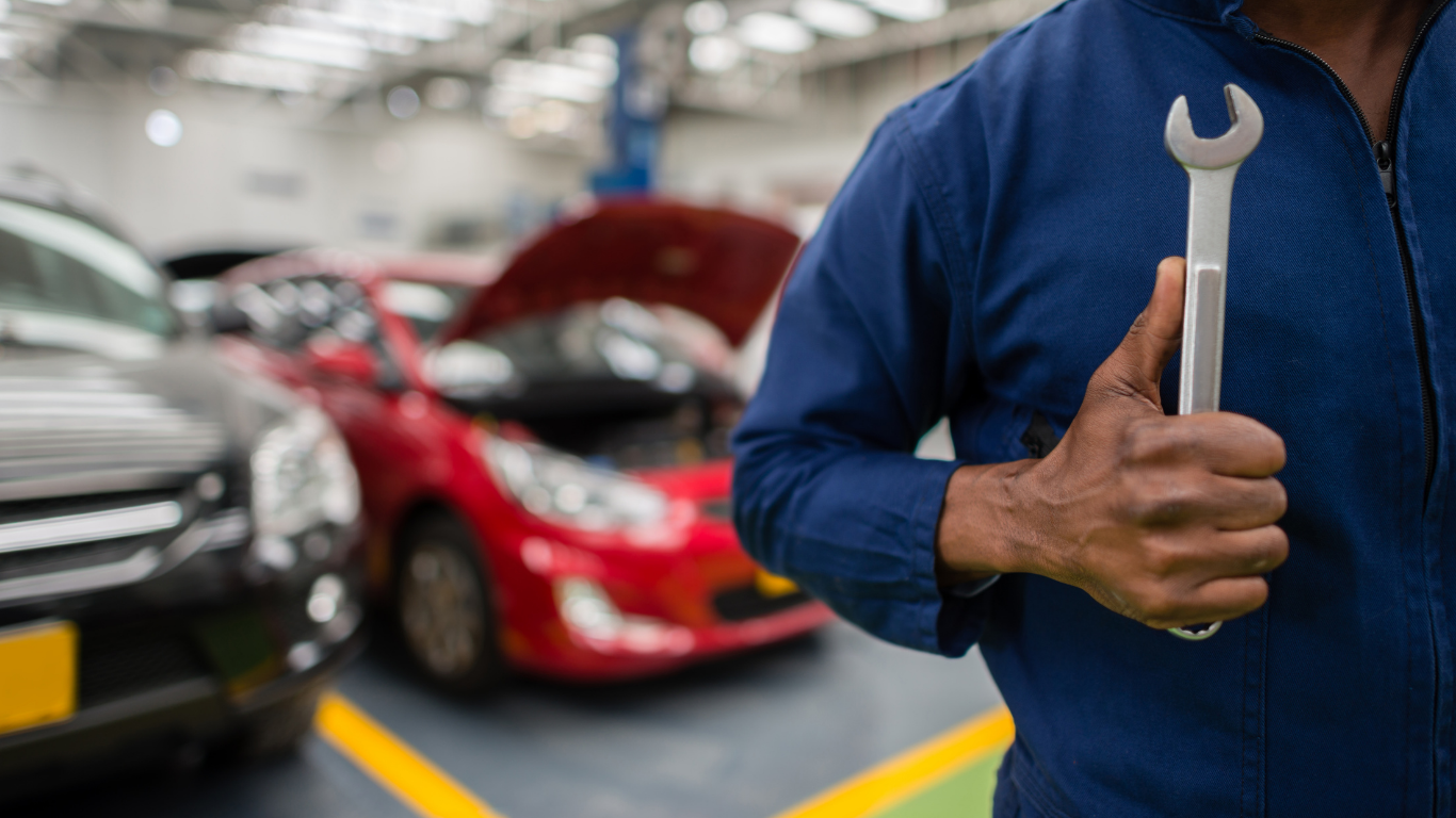 Mechanic holding a wrench in auto repair shop, with cars in the background.