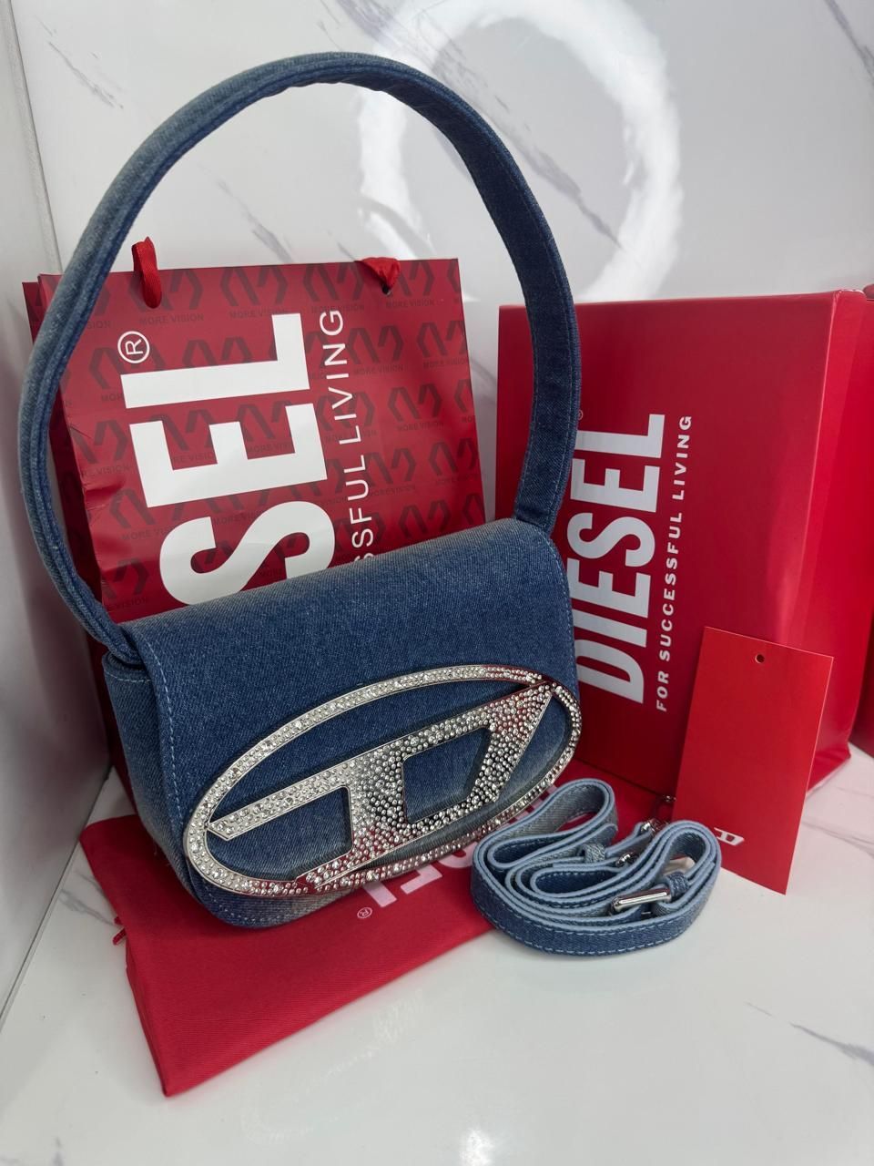 Bolso de mano Diesel en denim con logo "D" brillante, bolsas de compra rojas y correa.