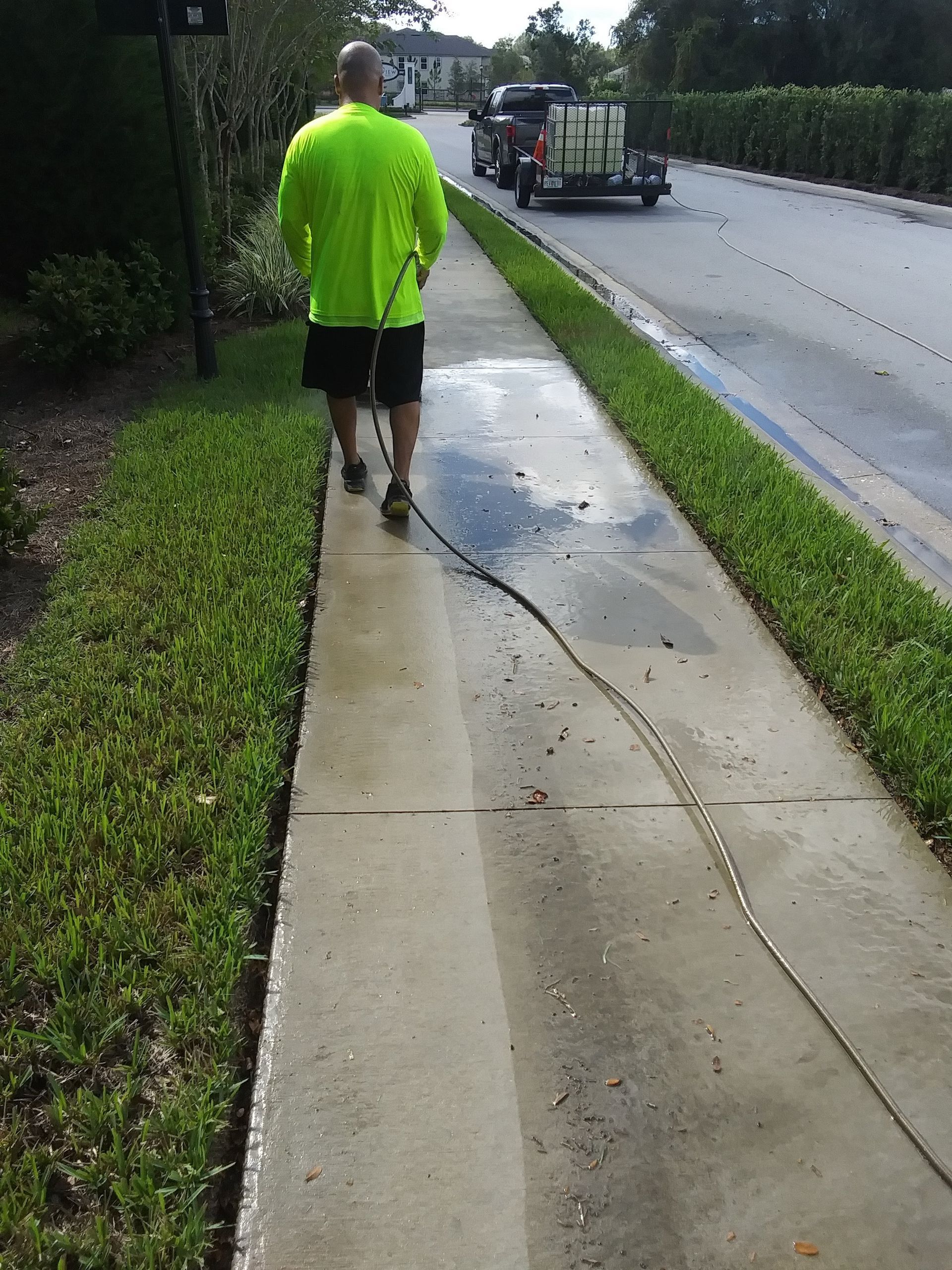 Man in neon green shirt power washing a concrete sidewalk.