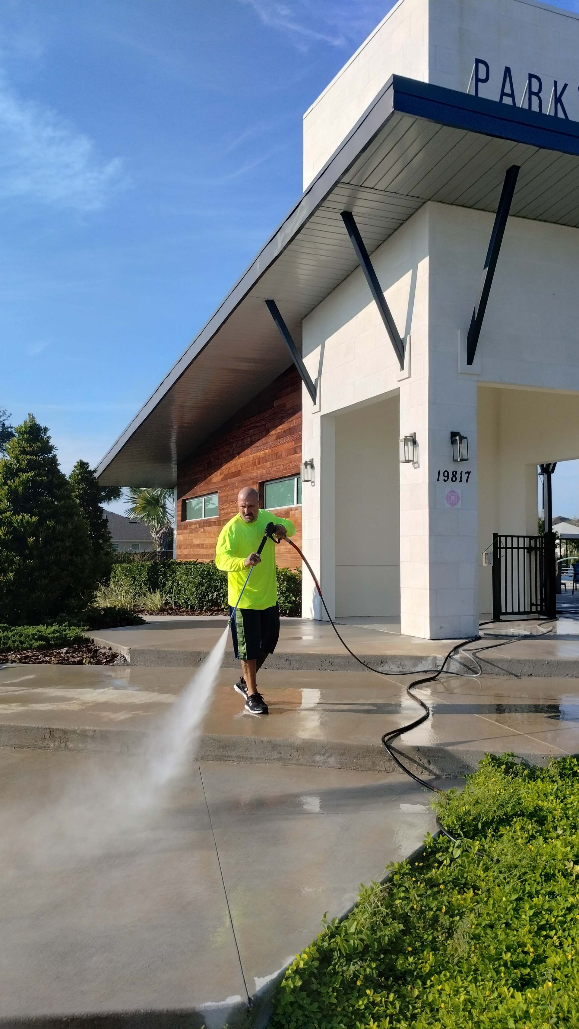 Man power washing a sidewalk in front of a building marked 