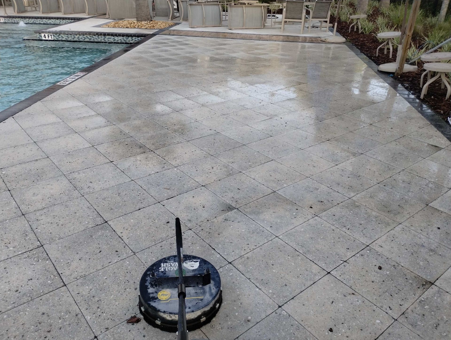 A pressure washer cleaning light gray patio pavers next to a pool.