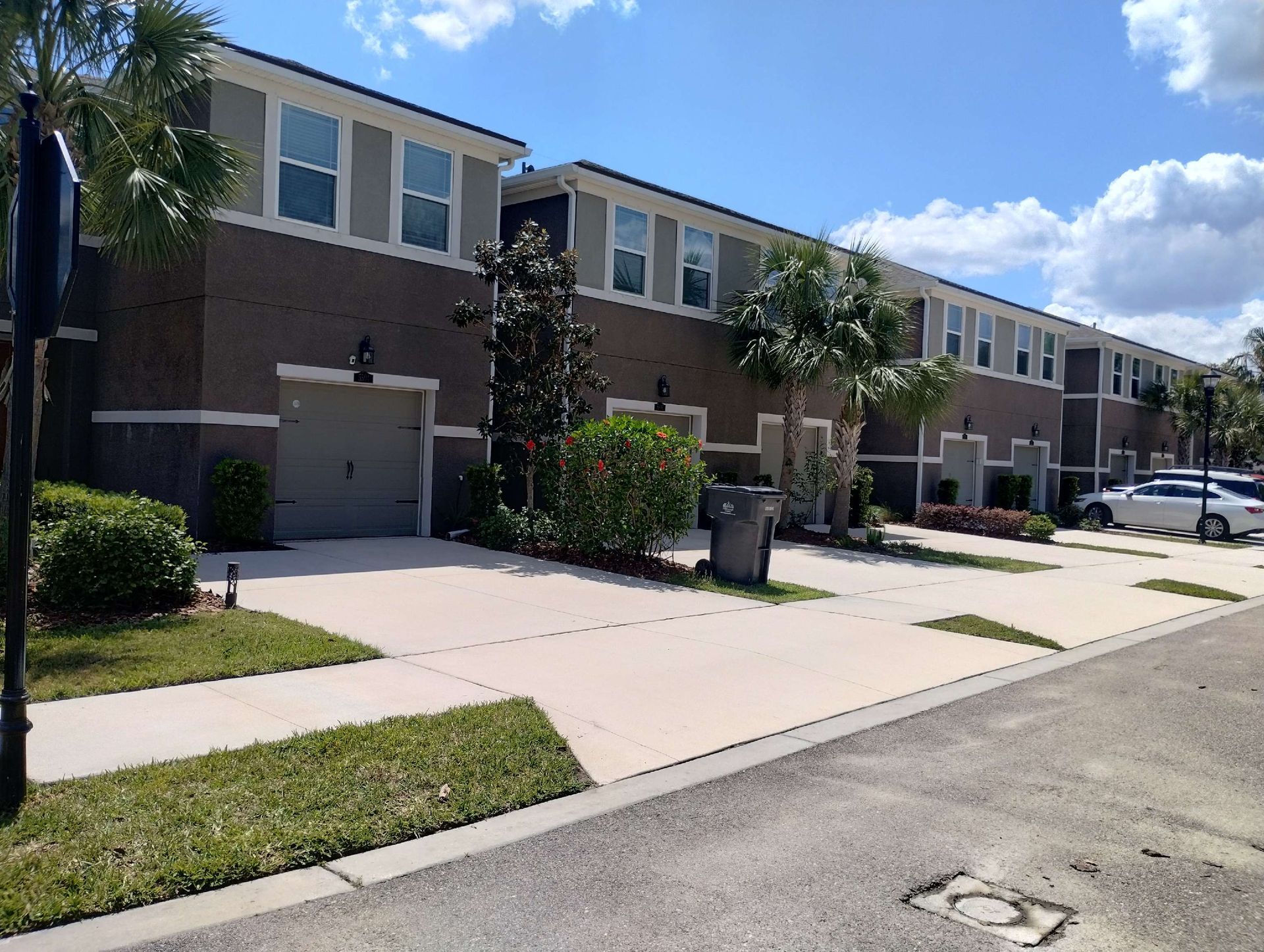 Row of townhomes with beige, gray, and brown exteriors; palm trees and parked cars in front.