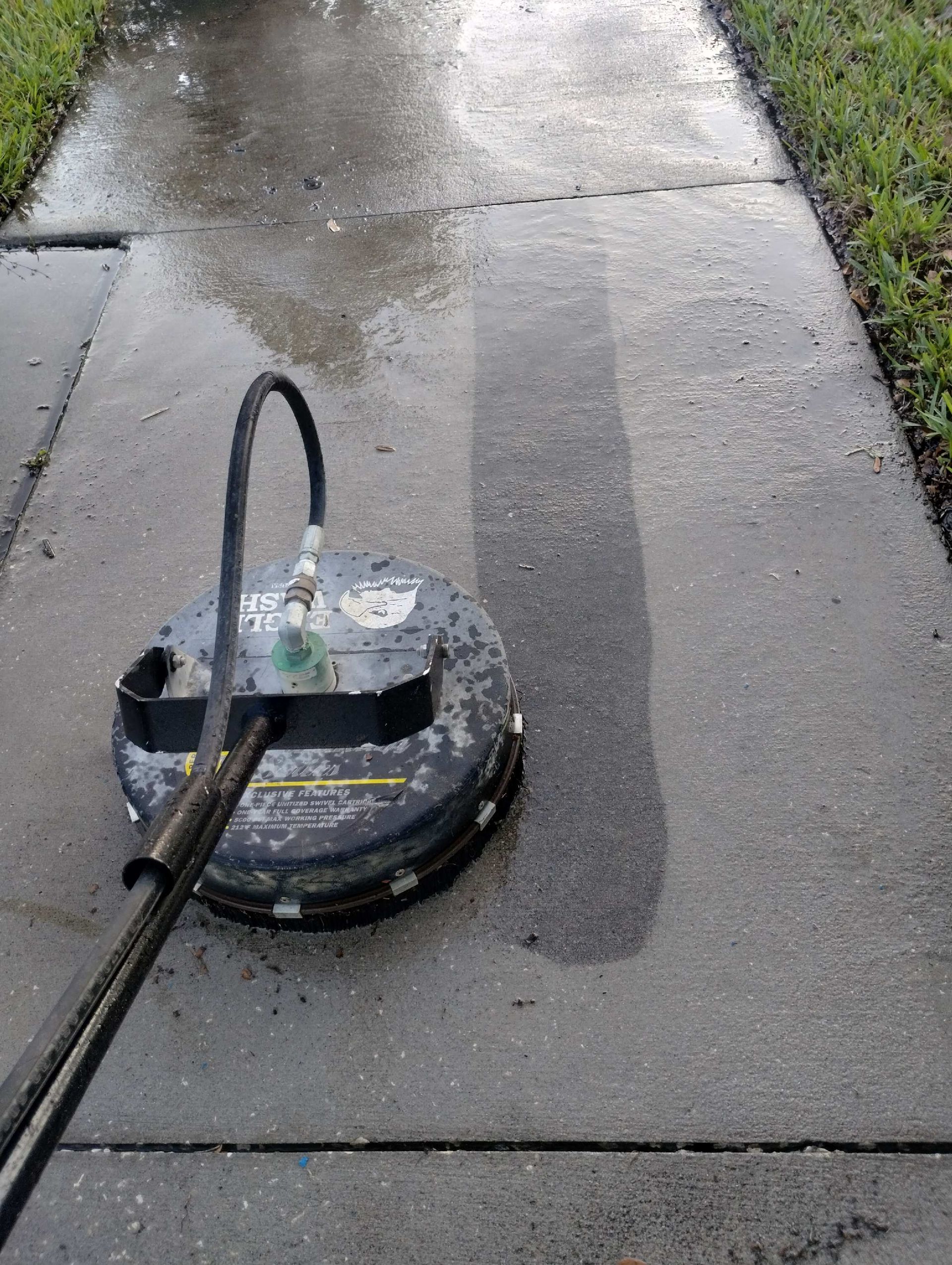 A pressure washer cleaning a concrete sidewalk, leaving a clean strip.