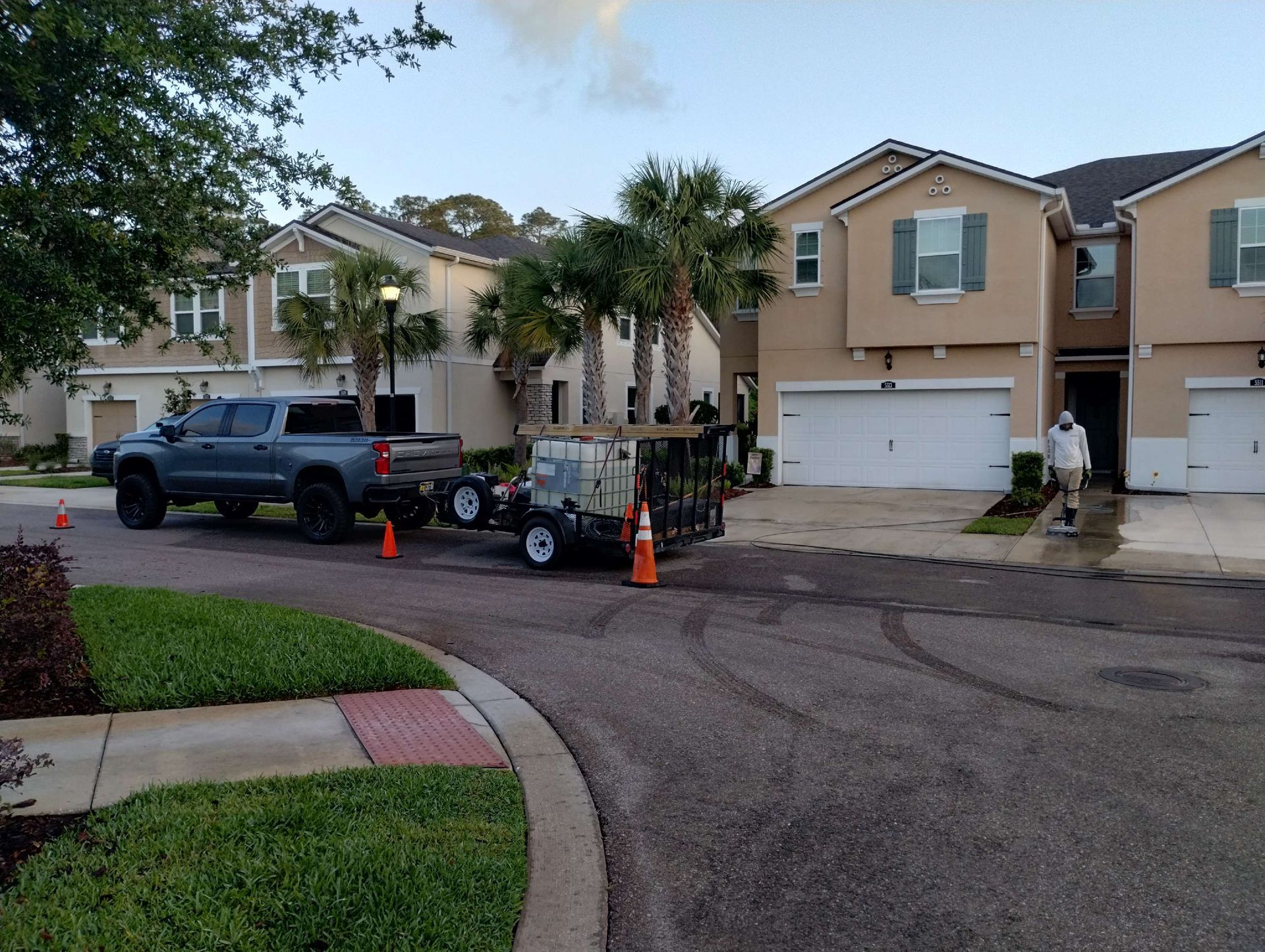 A truck pulling a trailer parked in front of a house; person spraying.