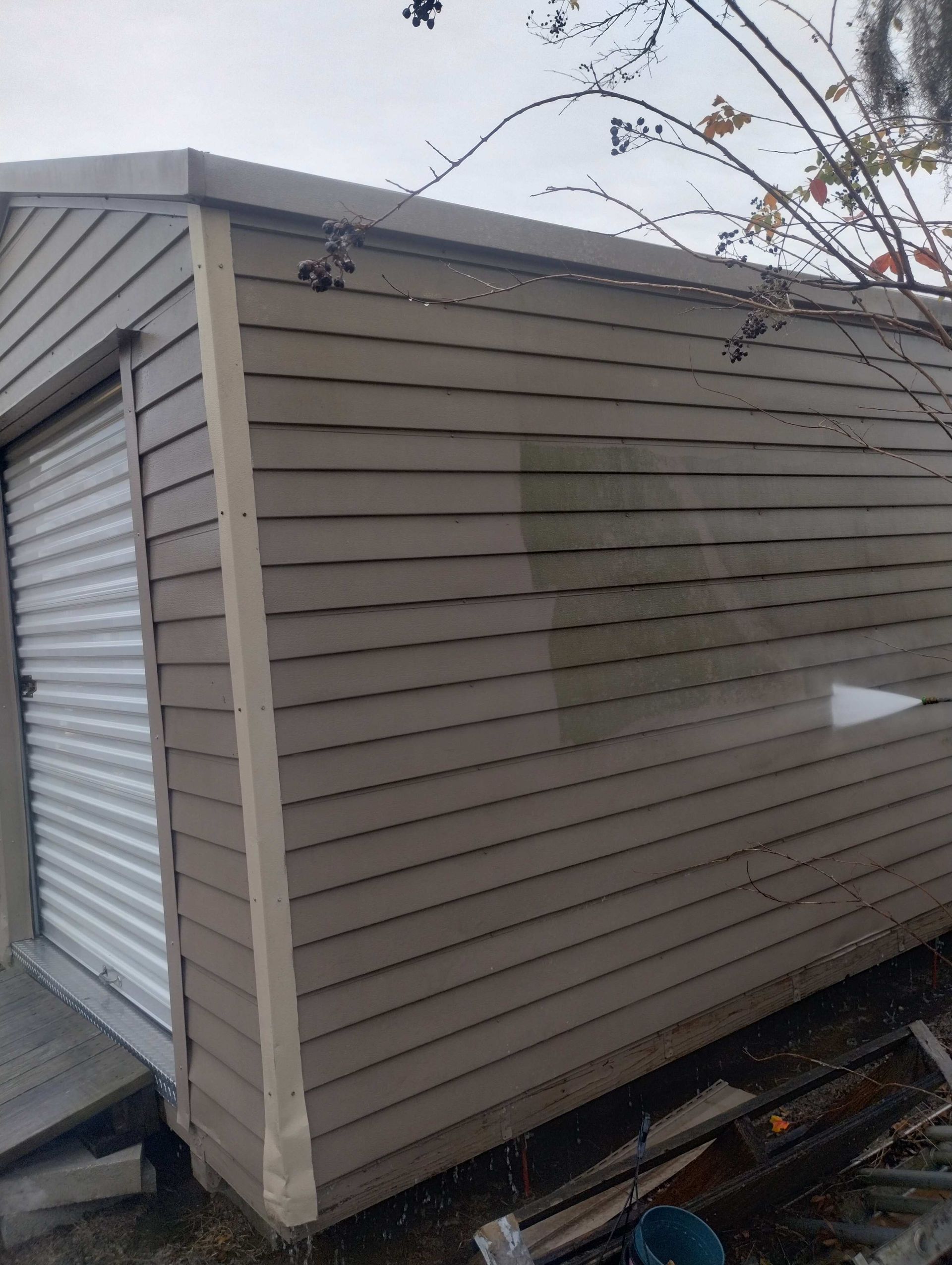 Tan shed with a white roll-up door and tan siding, next to a bare tree.