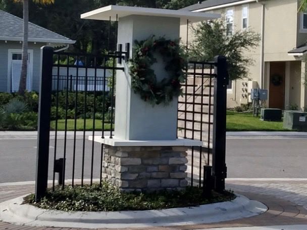 Monument entrance with a wreath, black metal fence, and stone base in a residential neighborhood.