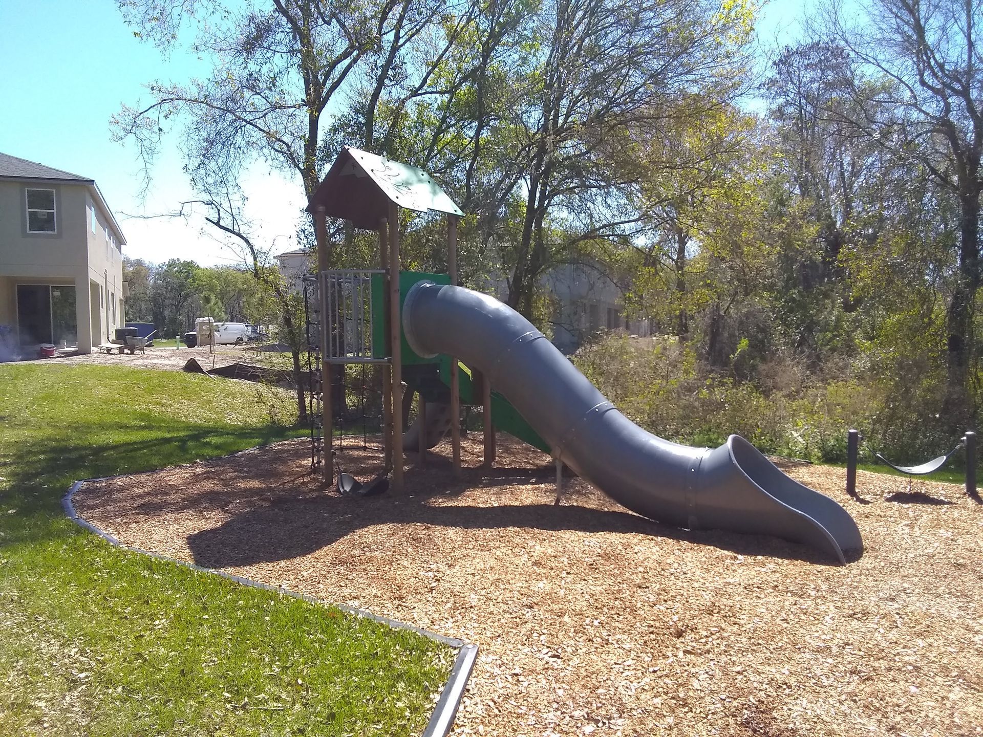 Playground with gray slide, wooden structure, and mulch ground.
